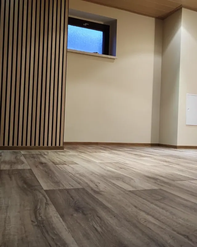 Wohnraum mit Holz-Lamellenwand, Vinyl-Designboden in Dielenoptik und holzverkleideter Dachschräge