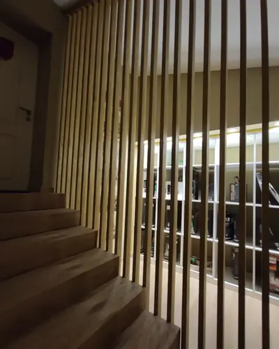 Treppenaufgang mit vertikalen Holzlamellen als Raumteiler und beleuchtetem Regal dahinter