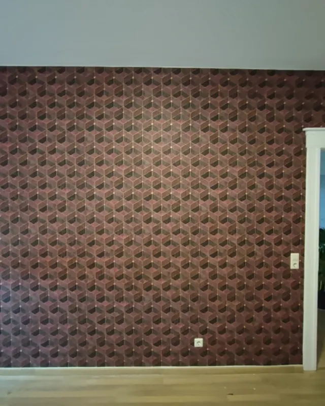 Wand mit geometrischem Würfelmuster in Rot- und Brauntönen über die gesamte Fläche, heller Dielenboden