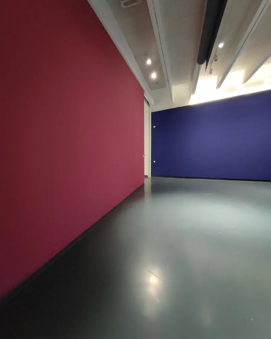 Der Raum mit den beiden Farbflächen aus flachem Winkel: rote Wand links, blaue Wand rechts, dazwischen die beleuchtete Deckenkante.