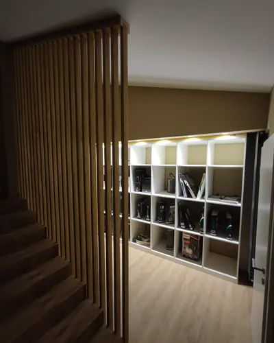 Lamellenwand neben der Treppe, rechts daneben ein raumhohes weißes Regalraster mit indirekter Beleuchtung in den Fächern.